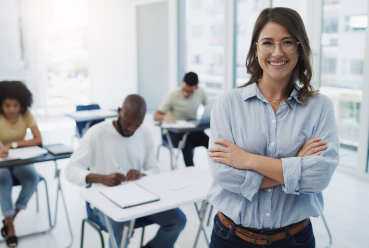 Education, portrait and woman professor in a classroom with students for teaching, knowledge and motivation. College, teacher and face of female leader happy in a class with group of people learning